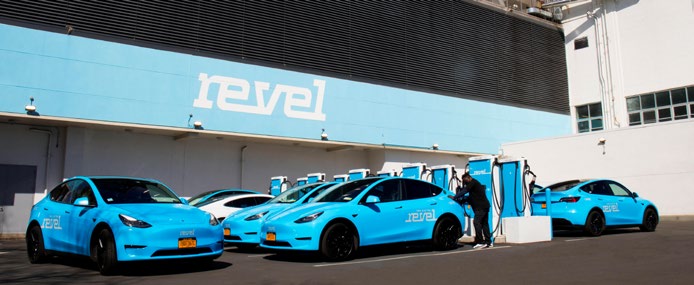 Fleet of blue Revel vehicles in front of charging stations.